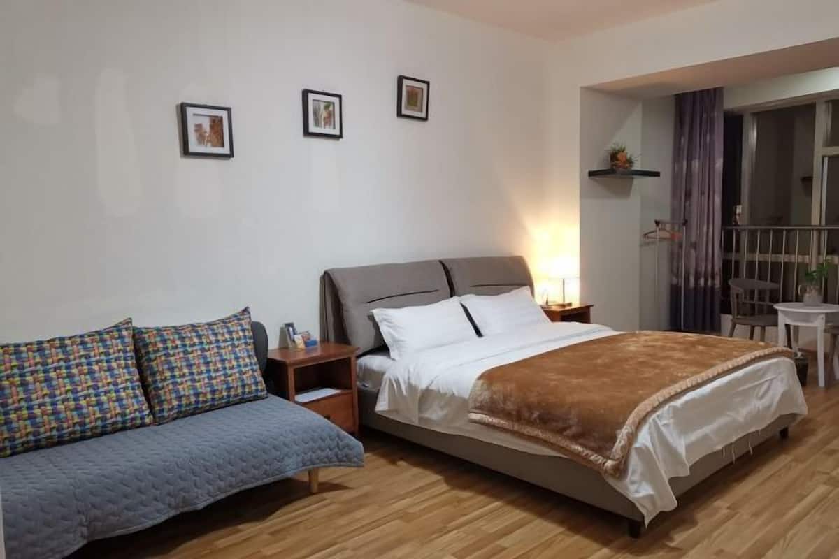 A bedroom with a bed, a sofa, a nightstand, and a small table.
