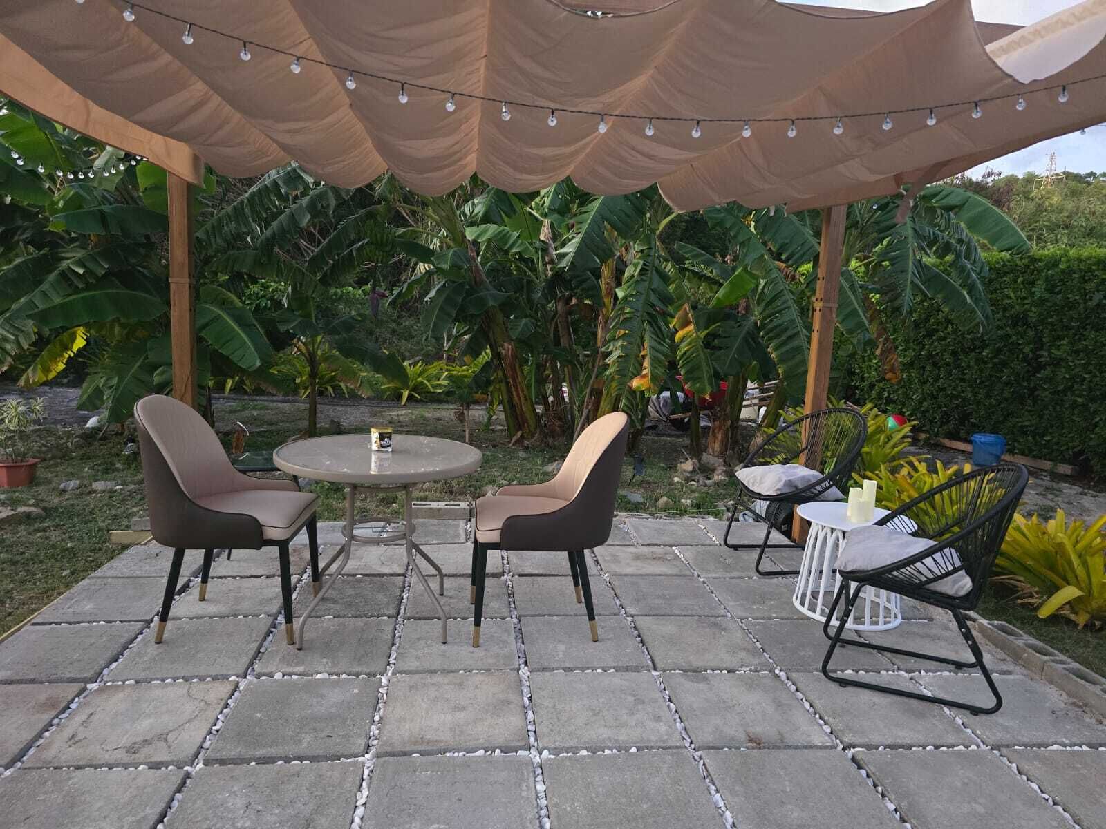 An outdoor patio with a round table and two chairs, surrounded by a pergola with string lights.