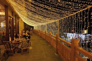 An indoor walkway with string lights, wooden railings, and tables with chairs.