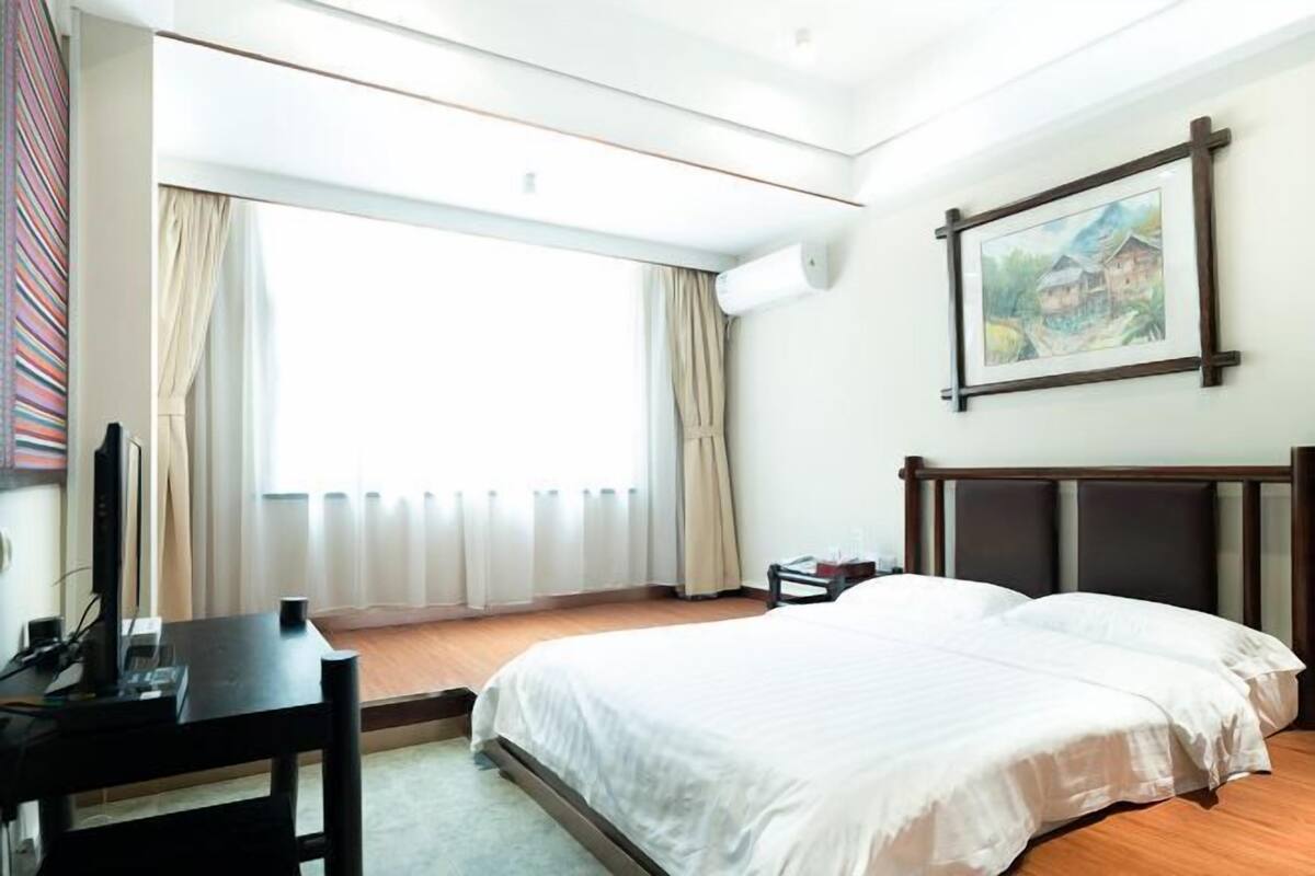 Ein Hotelzimmer mit Bett, Schreibtisch, Stuhl, Fernseher und einem fensterbepflanzten Fenster.