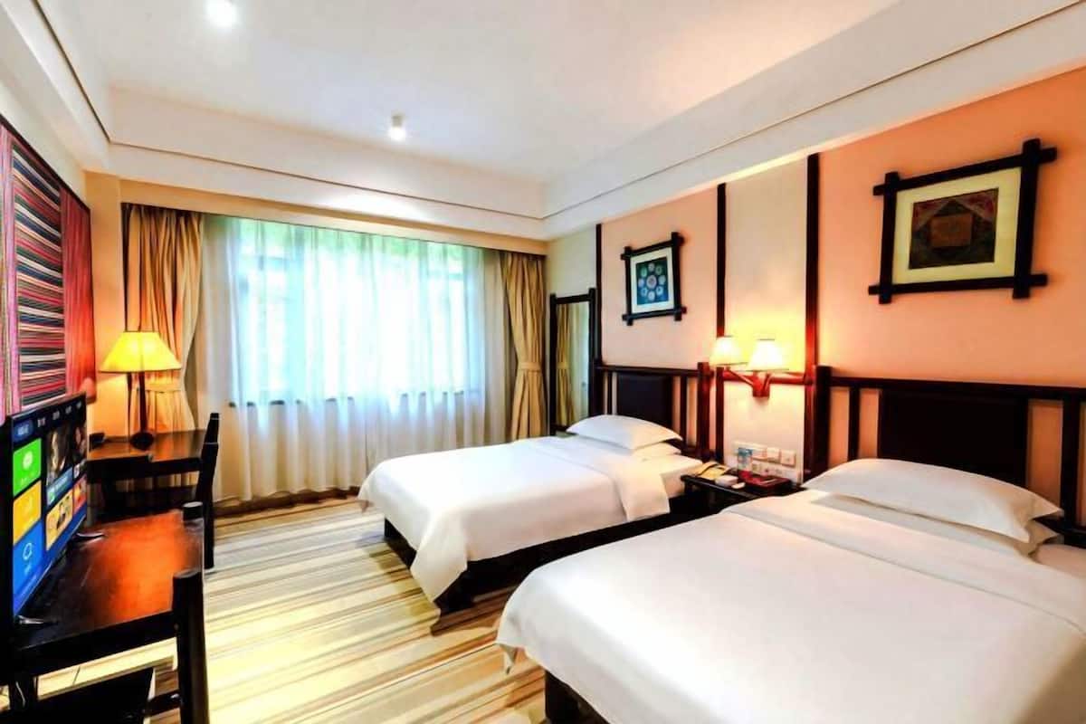 Ein Hotelzimmer mit zwei Betten, einem Schreibtisch mit Computer, einem Fernseher und einem Fenster mit Vorhängen.