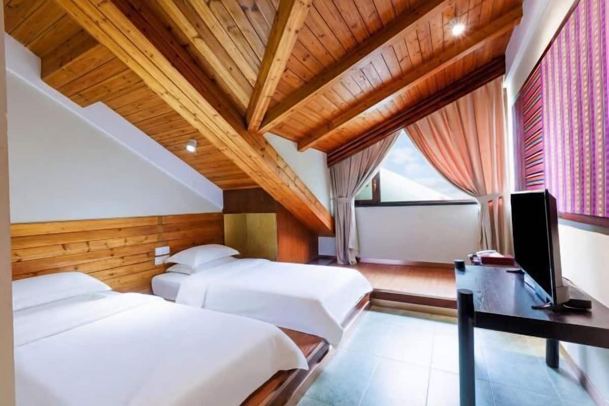 Ein Hotelzimmer mit zwei Betten, Holzbalkendecke, einem Fernseher und einem mit Vorhängen versehenen Fenster.