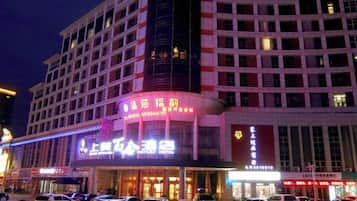 A multi-story hotel with illuminated signage, a parking lot, and a busy street at night.