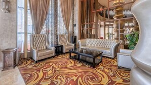 A spacious living room with a patterned carpet, a sofa, armchairs, a coffee table, and a decorative bookshelf. - Beau Upward Maylily Hotel (Yinchuan)