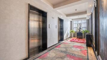 A hotel corridor with elevators, a patterned carpet, and a view into a room with a large window.