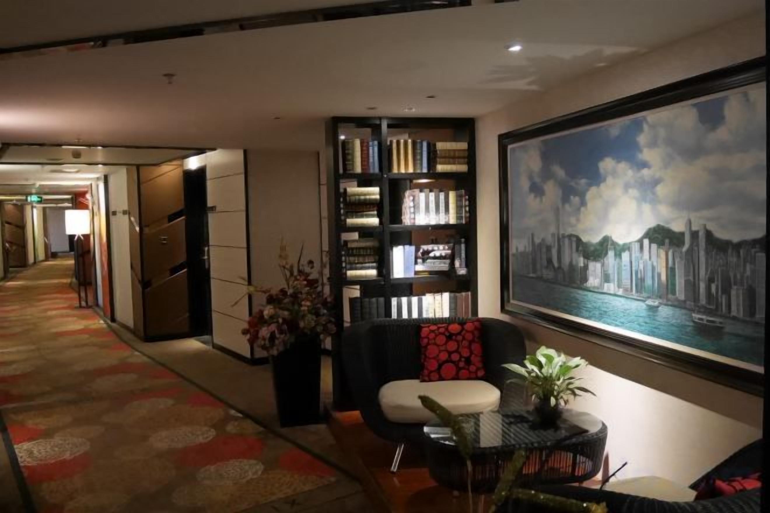 A hotel lobby with a bookshelf, a seating area, and a large painting of a cityscape.