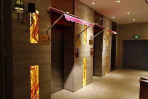 Un couloir au design moderne, agrémenté d’une série d’ascenseurs dotés d’auvents rouges et de panneaux lumineux.