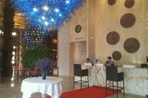 A hotel lobby with a reception desk, chairs, a red carpet, and a decorative plant.