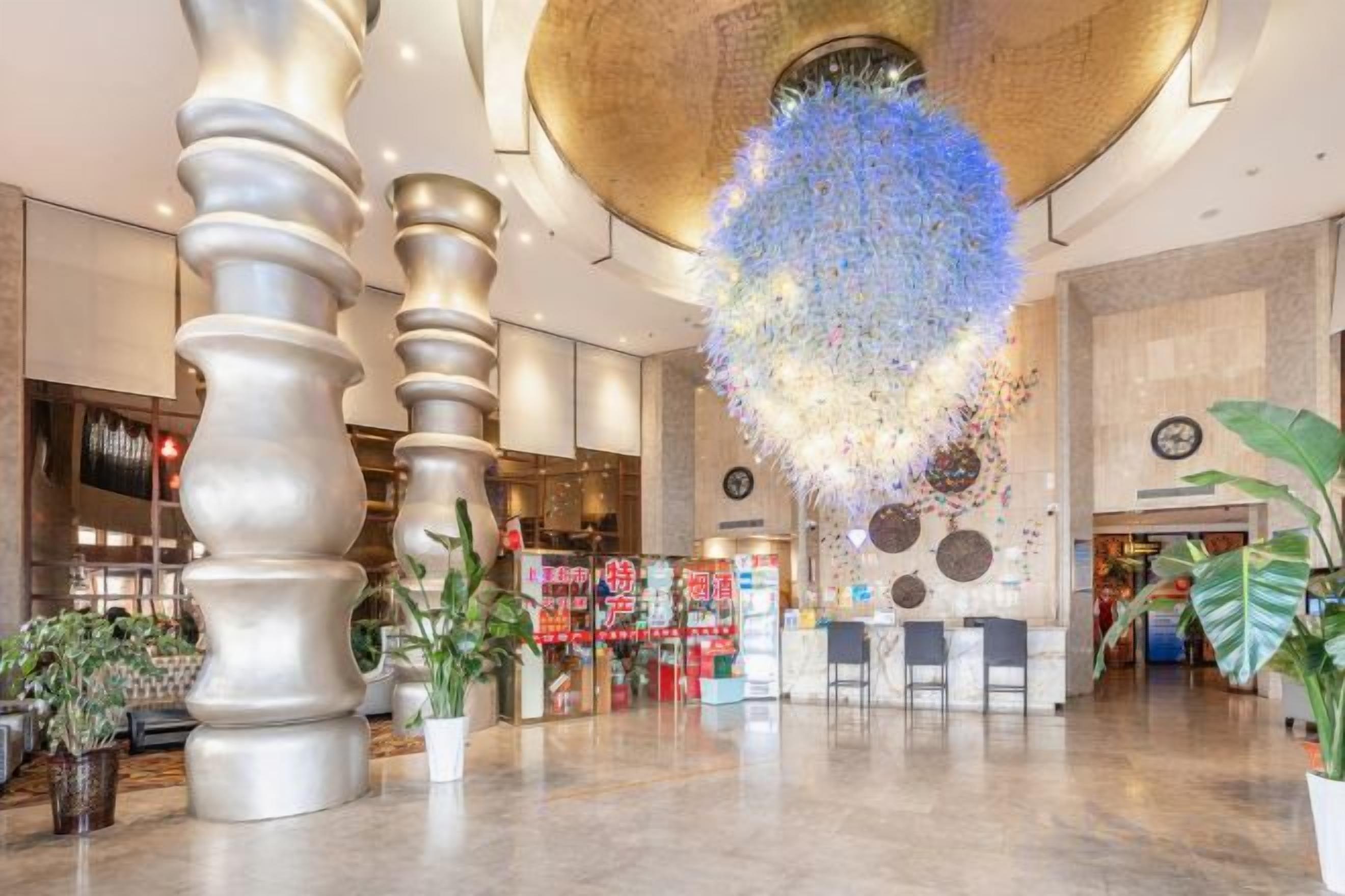 A spacious lobby with a unique ceiling design, a reception area, and potted plants.
