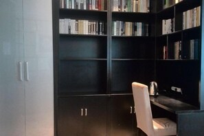 A room with a dark bookshelf, a white chair, and a desk with a kettle.