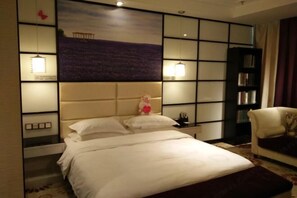 A hotel room with a bed, a nightstand, a bookshelf, and a wall with a painting. - Beau Upward Maylily Hotel (Yinchuan)