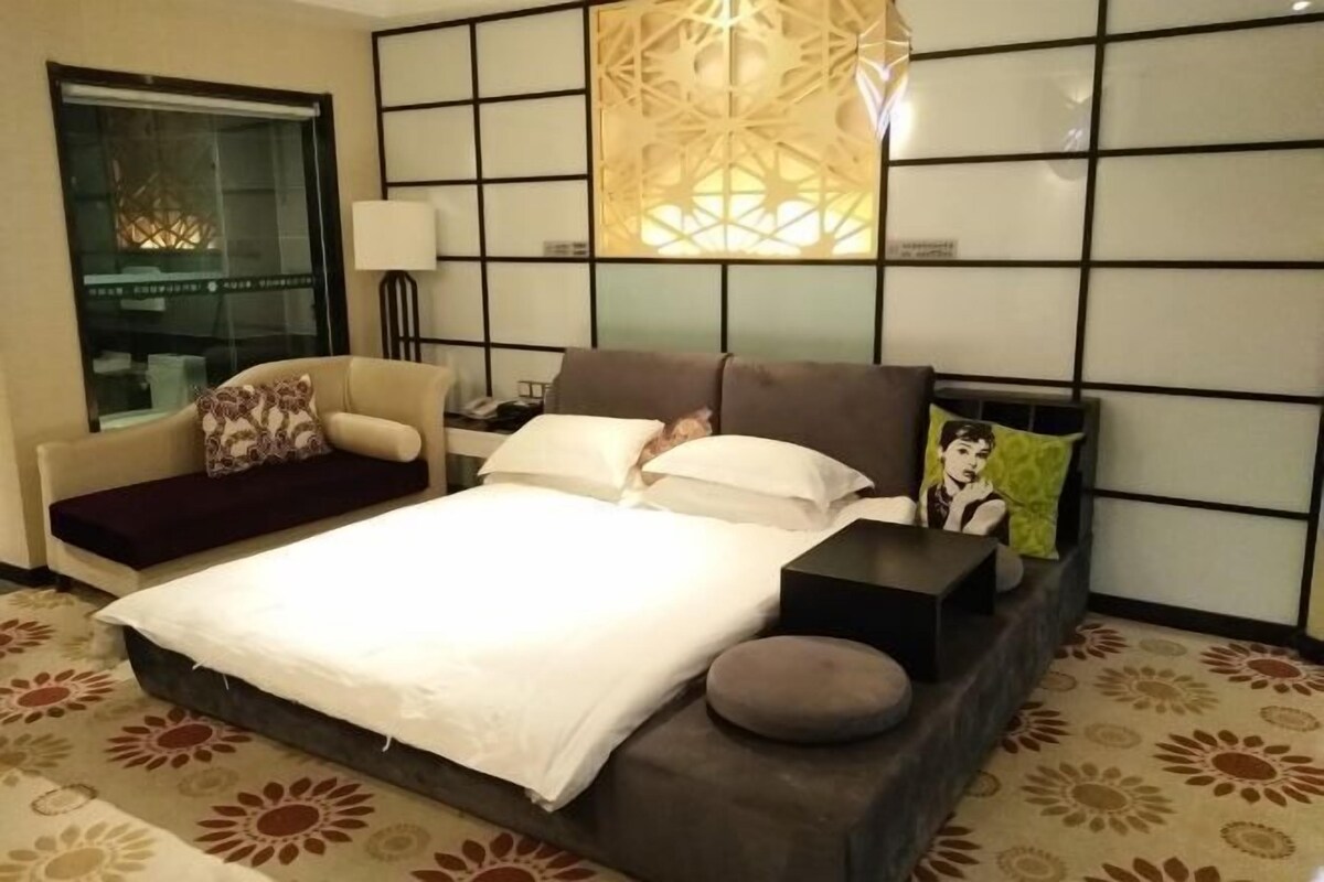 A modern hotel room with a large bed, a sofa, a nightstand, and a decorative wall panel.