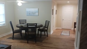 A dining area with a round table and chairs, a ceiling fan, and a painting on the wall. - Recently updated cottage minutes from beach, pet friendly, large yard wifi, ac (Longs)