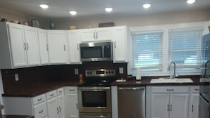 A modern kitchen with white cabinets, stainless steel appliances, and a wooden floor. - Recently updated cottage minutes from beach, pet friendly, large yard wifi, ac (Longs)