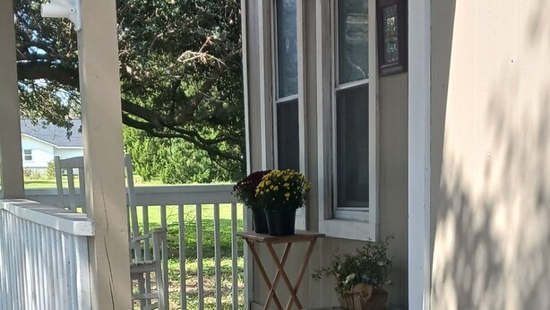 A wooden porch with steps leading to a house, a small wooden table, and potted plants. - Recently updated cottage minutes from beach, pet friendly, large yard wifi, ac (Longs)