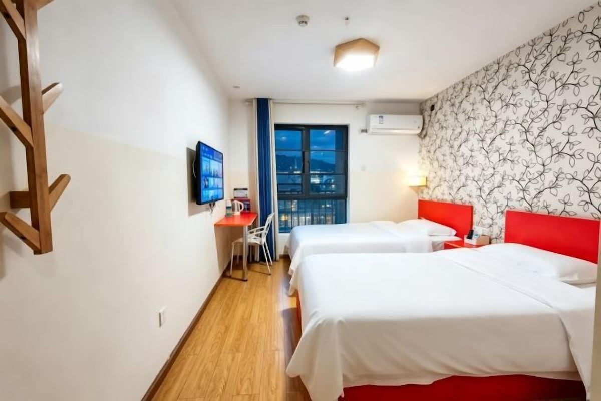 Une chambre d’hôtel avec deux lits, un bureau avec une chaise, une télévision et une fenêtre donnant sur un paysage agréable.