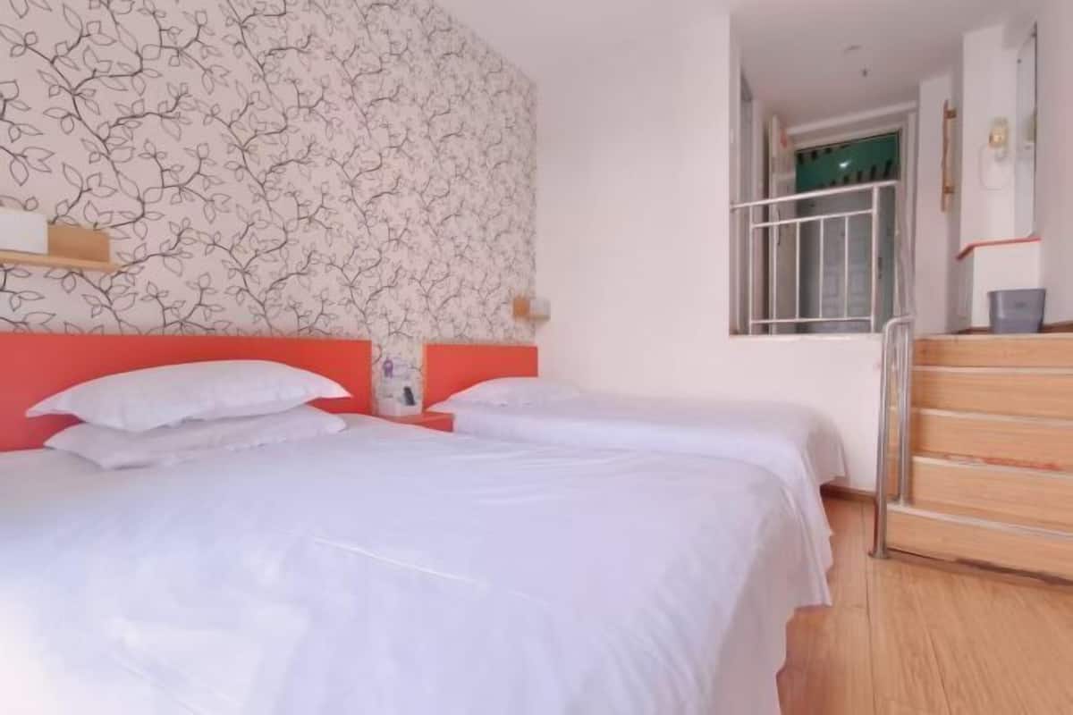 Ein Hotelzimmer mit zwei Betten, einem roten Kopfteil, einer Wand mit Muster und einem Fenster mit Metallgitter.
