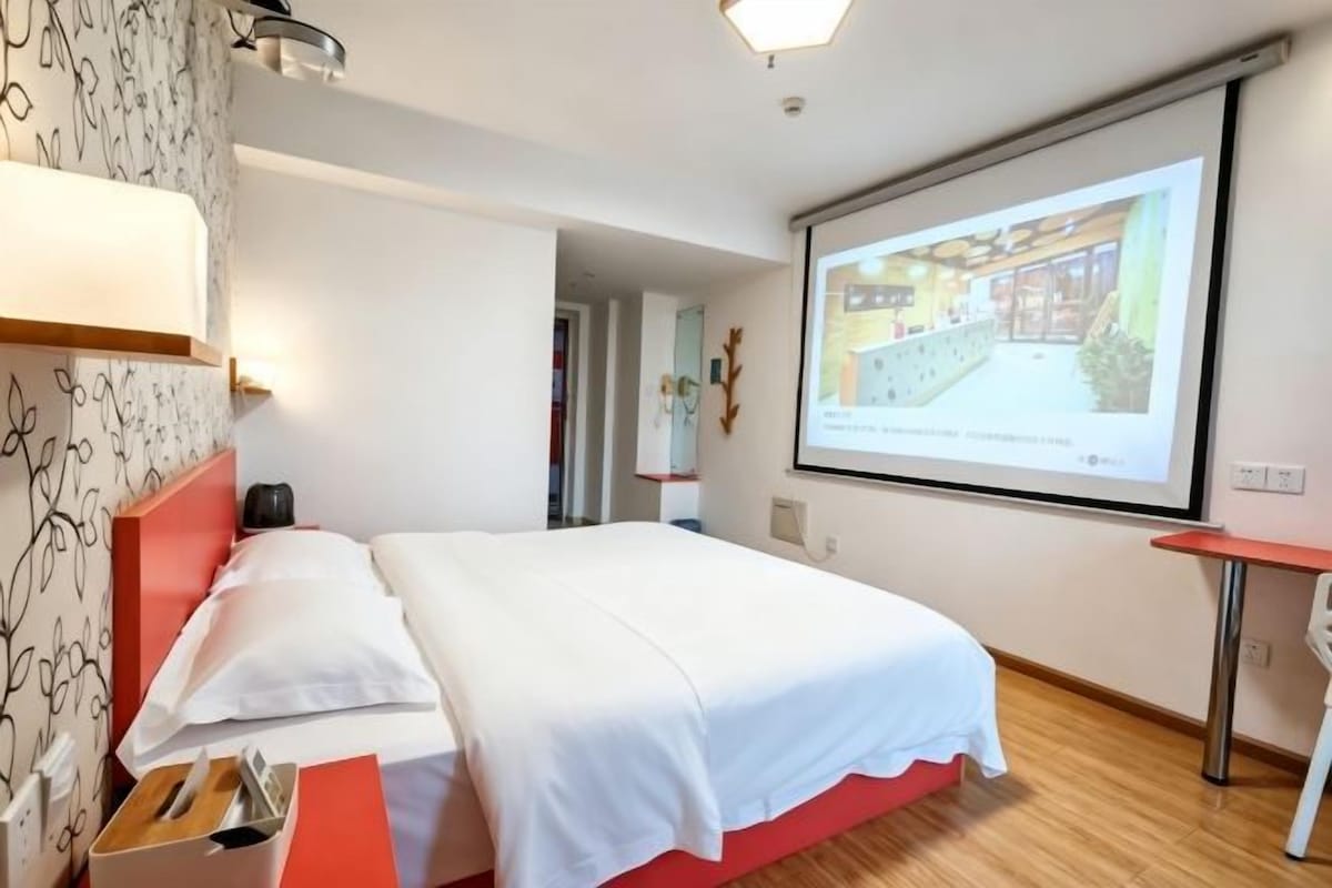 Une chambre d’hôtel équipée d’un lit, d’un bureau, d’un écran de projection et d’un téléviseur fixé au mur.