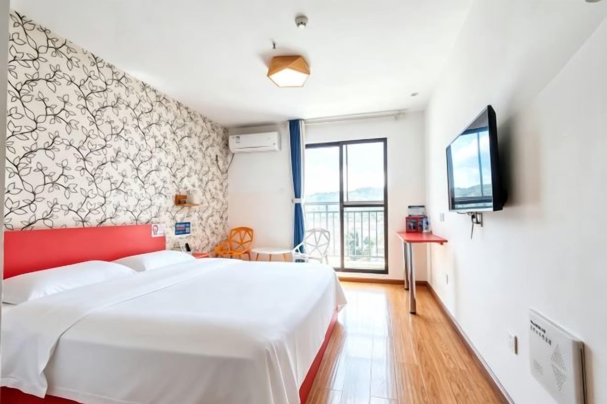 Une chambre d’hôtel équipée d’un lit, d’une télévision, d’un balcon et offrant une vue sur l’extérieur.