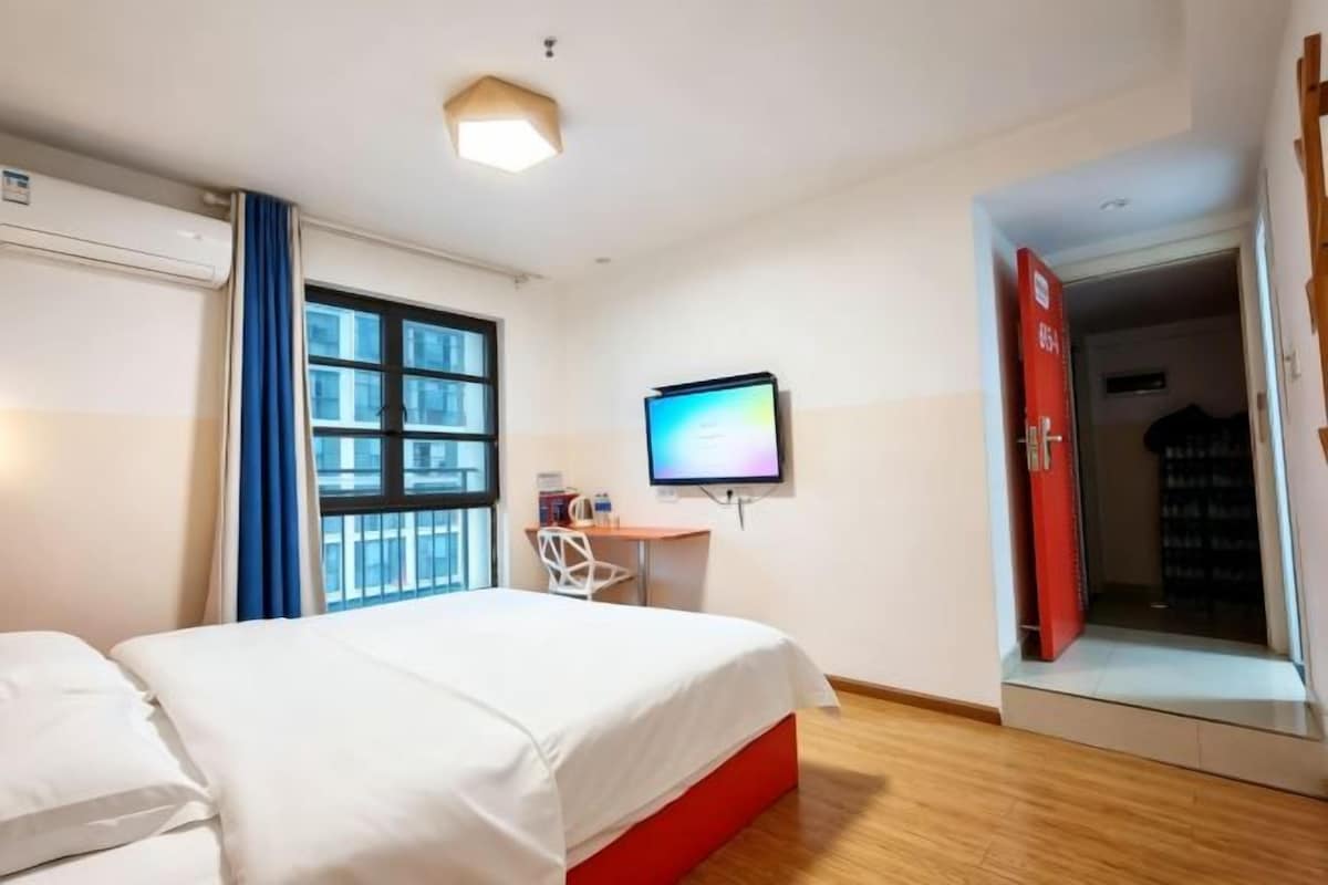 Une chambre d’hôtel comprenant un lit, un bureau avec un ordinateur, une fenêtre avec des rideaux et une porte donnant sur une autre pièce.