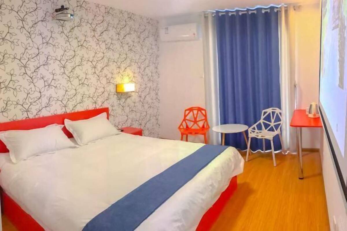 Ein Hotelzimmer mit Bett, einem kleinen Tisch, zwei Stühlen, einer Wand-Klimaanlage und einem Fenster mit Vorhängen.