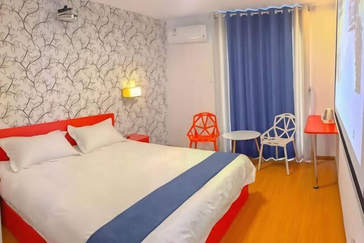 Ein Hotelzimmer mit Bett, einem kleinen Tisch, zwei Stühlen, einer Wand-Klimaanlage und einem Fenster mit Vorhängen.