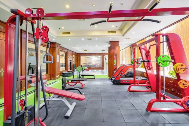 Een sportschool met diverse fitnessapparaten, waaronder krachtapparaten en banken.