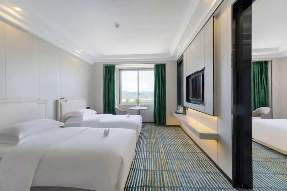 Quarto de hotel com duas camas, televisão, uma mesinha e vista para o exterior.