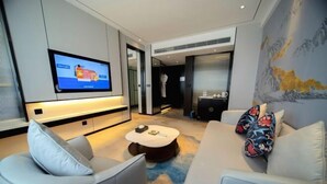 A modern living room with a flat-screen TV, a round coffee table, and a sofa with decorative pillows. - Light Grand Hotel (Fengdu County)