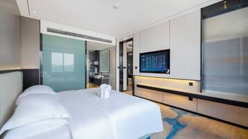 Ein modernes Hotelzimmer mit einem großen Bett, einem flachbildfernseher an der Wand und einer Glastür zum Badezimmer.