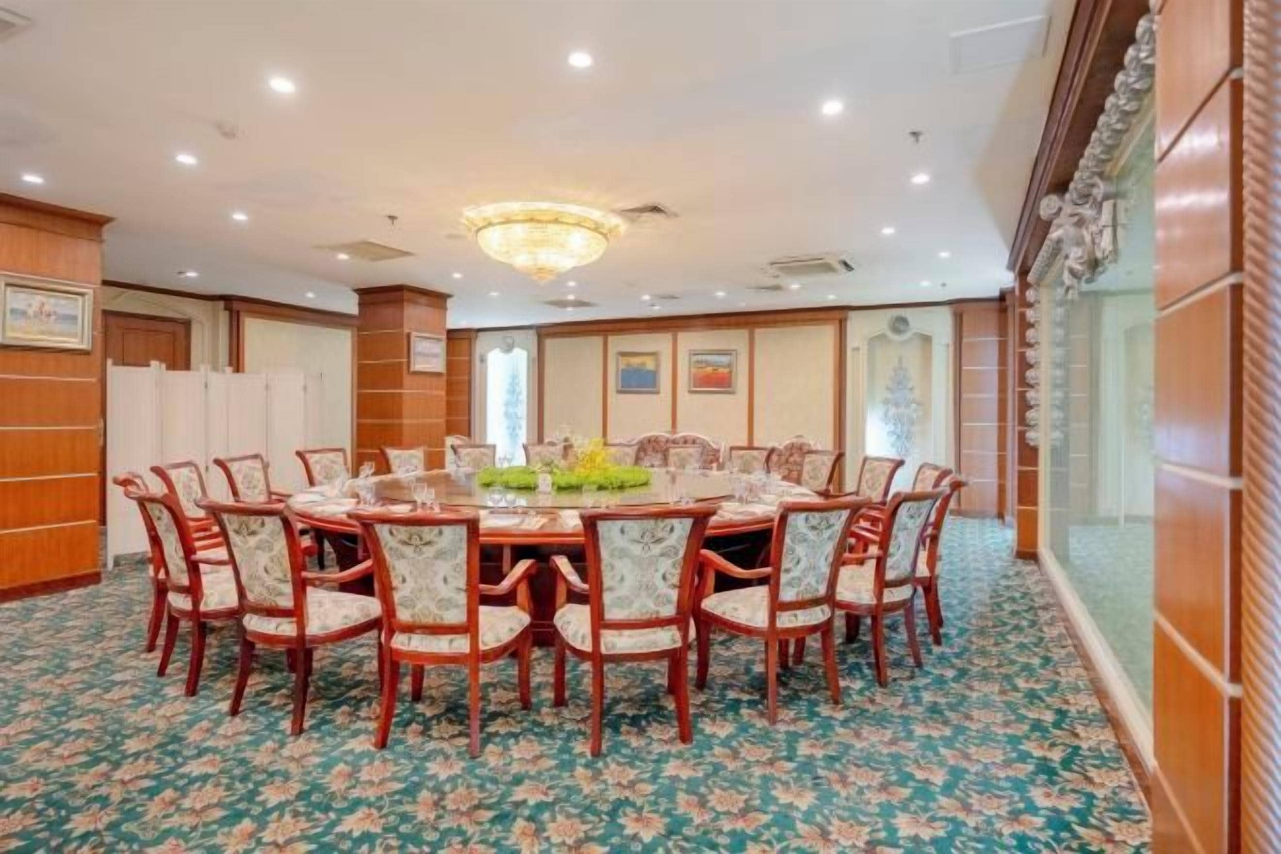 A conference room with a round table surrounded by chairs, a chandelier, and a patterned carpet.
