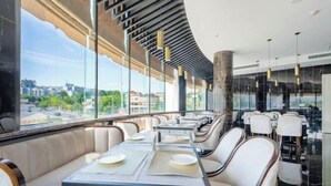 A modern restaurant with a curved ceiling, large windows offering a city view, and a mix of seating options including tables and booths. - Light Grand Hotel (Fengdu County)