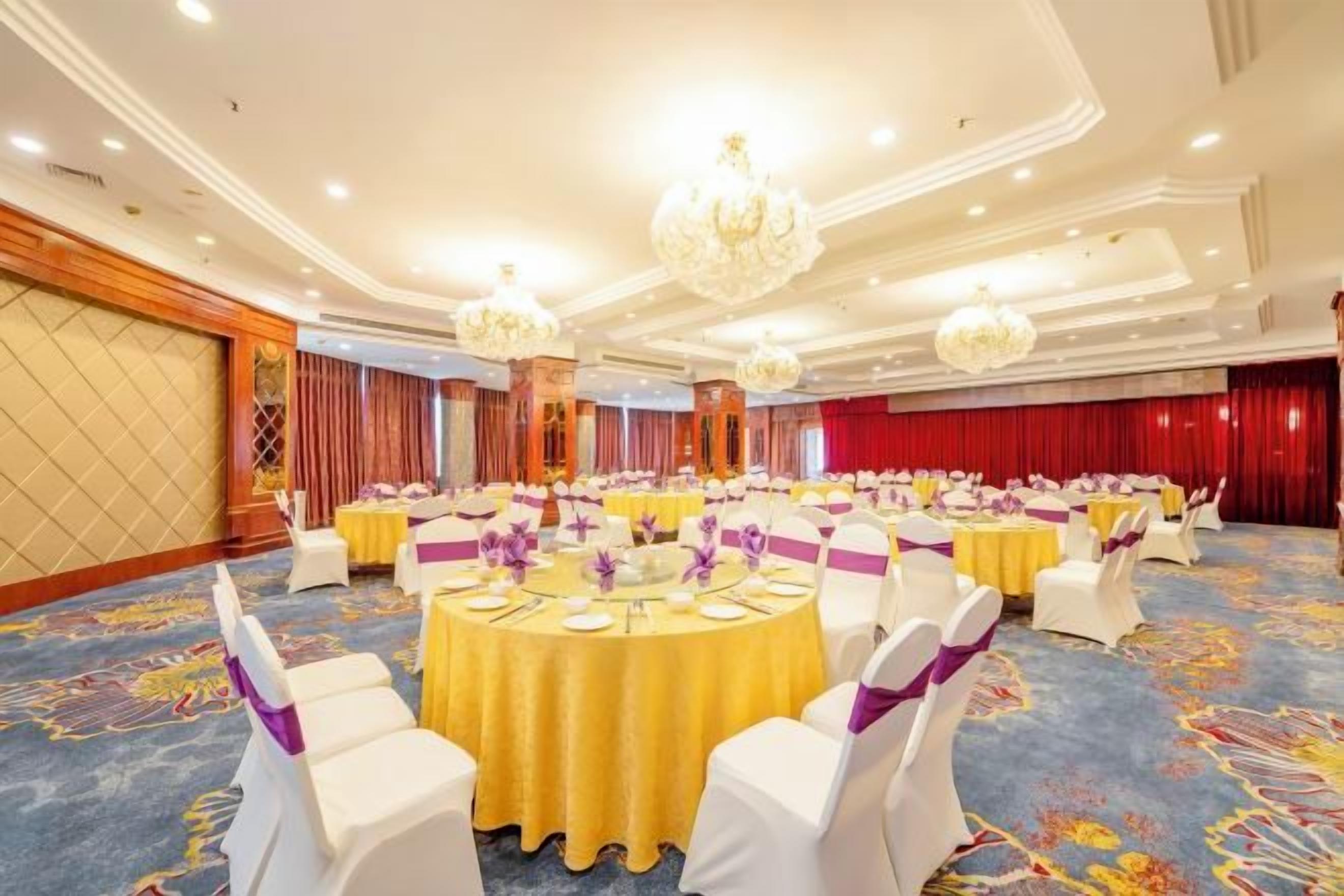 A banquet hall with round tables, white chairs, and chandeliers.