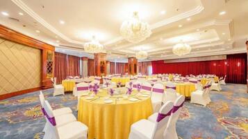 A banquet hall with round tables, white chairs, and chandeliers.