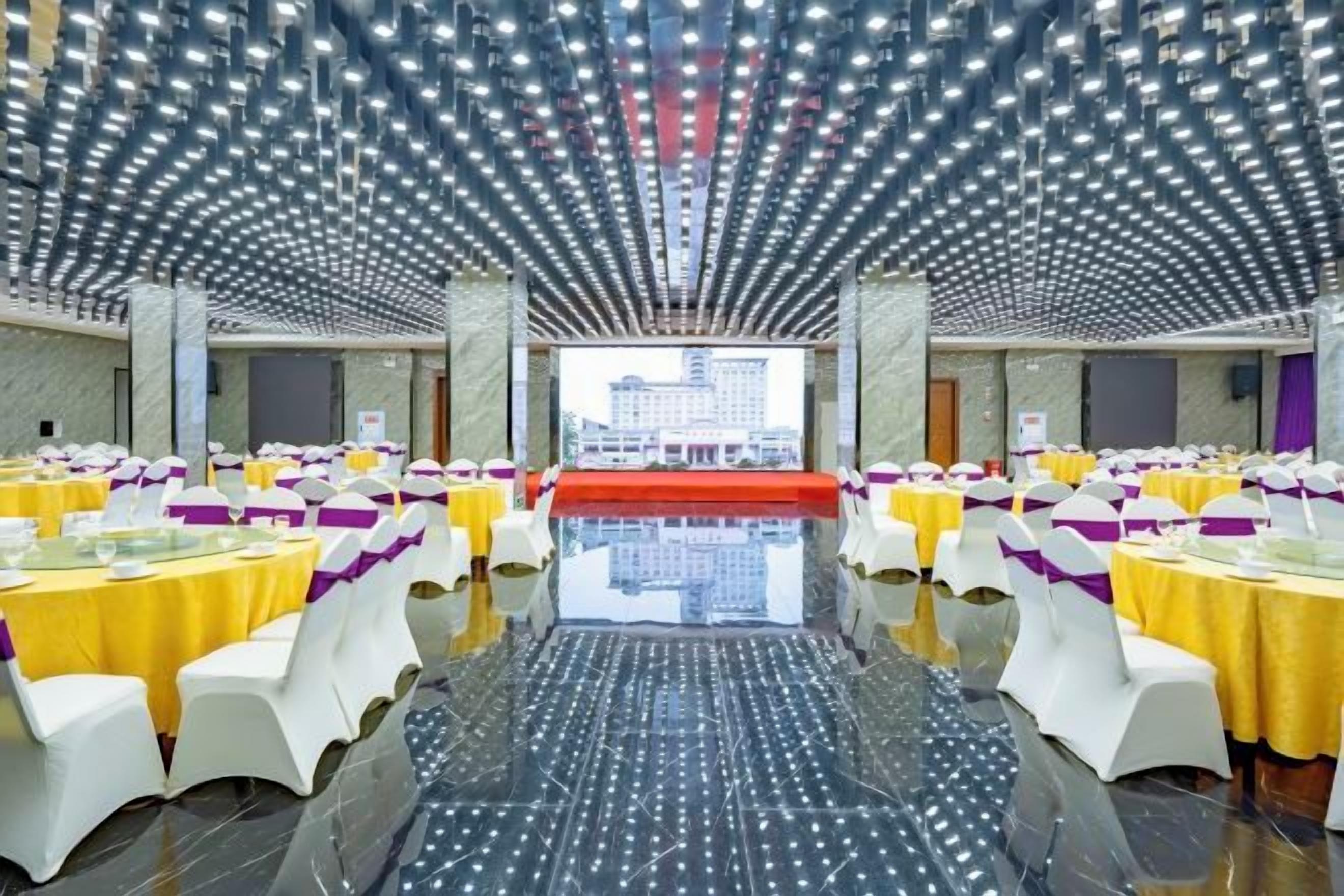 A banquet hall with tables arranged in rows, a polished floor, and a ceiling with a unique light fixture design.