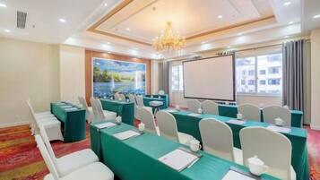 A conference room with long tables, chairs, a projector screen, and a painting on the wall.