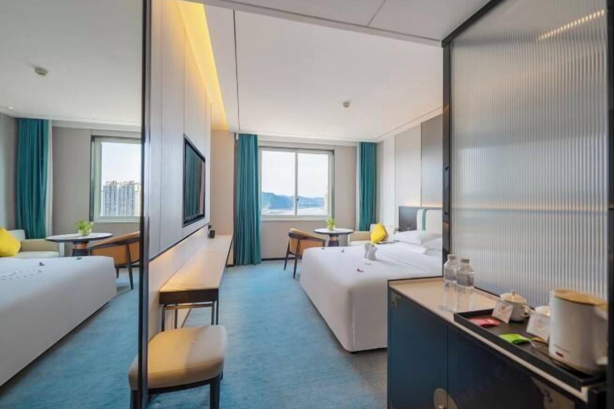 Quarto de hotel com duas camas, uma escrivaninha, uma cadeira, uma televisão e uma janela com vista.