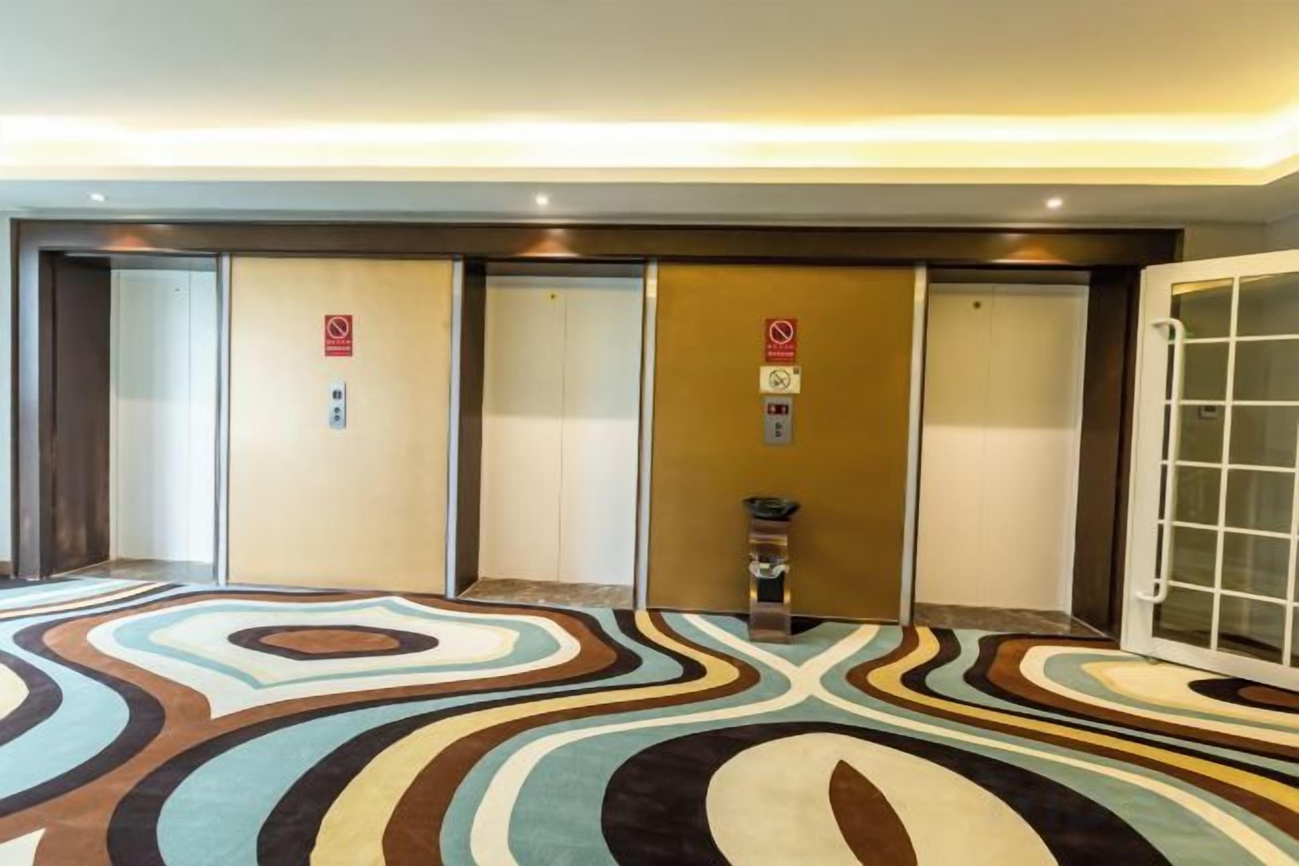 A hotel lobby with a patterned carpet, three elevators, and a reception desk.
