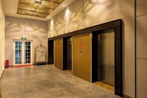 A hallway with three elevators, a trash bin, and a door with a glass panel. - Zhehui Hotel (Zhongshan)