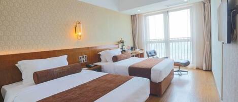 A hotel room with two beds, a desk, a chair, a TV, and a window with curtains.