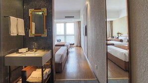 A hotel room with a large mirror, a sink, a bedside table, a bench, and a bed with a headboard. - Zhehui Hotel (Zhongshan)