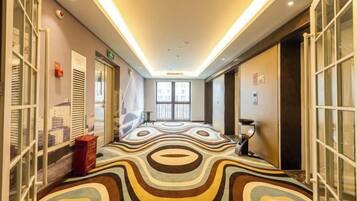 Un couloir d’hôtel avec un tapis à motifs, des portes en verre et une vue sur la ville.