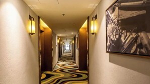 A hotel hallway with a patterned carpet, wall sconces, and a framed picture on the right wall. - Zhehui Hotel (Zhongshan)