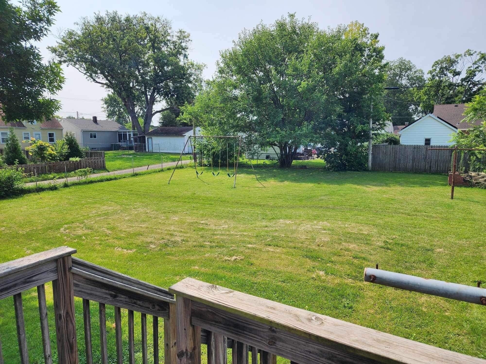 A backyard with a wooden deck, a swing set, and a fenced area.