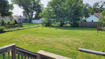 A backyard with a wooden deck, a swing set, and a fenced area.