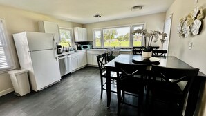 Une cuisine moderne avec des meubles blancs, une table à manger avec des chaises et une vue sur l’extérieur grâce à de grandes fenêtres.