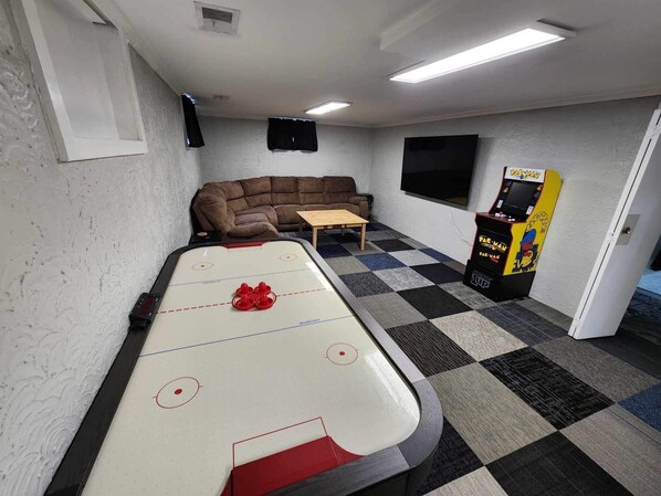 A room with a pool table, a sofa, a small table, and a Pac-Man arcade machine.