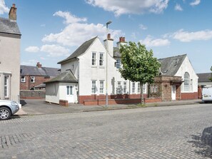 Une maison traditionnelle à deux étages, avec une façade en briques, des éléments décoratifs blancs et un grand arbre devant.