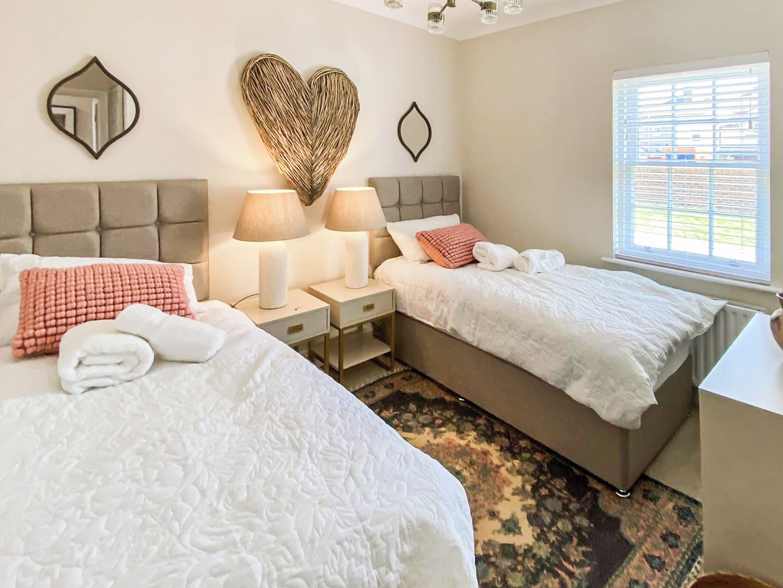Une chambre d’hôtel avec deux lits, une grande décoration murale en forme de cœur, une fenêtre avec des stores et un miroir sur le mur.
