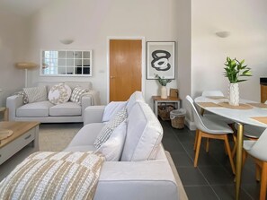 Un salon moderne avec un canapé, une table à manger et des chaises, une porte en bois et une œuvre d’art encadrée accrochée au mur.